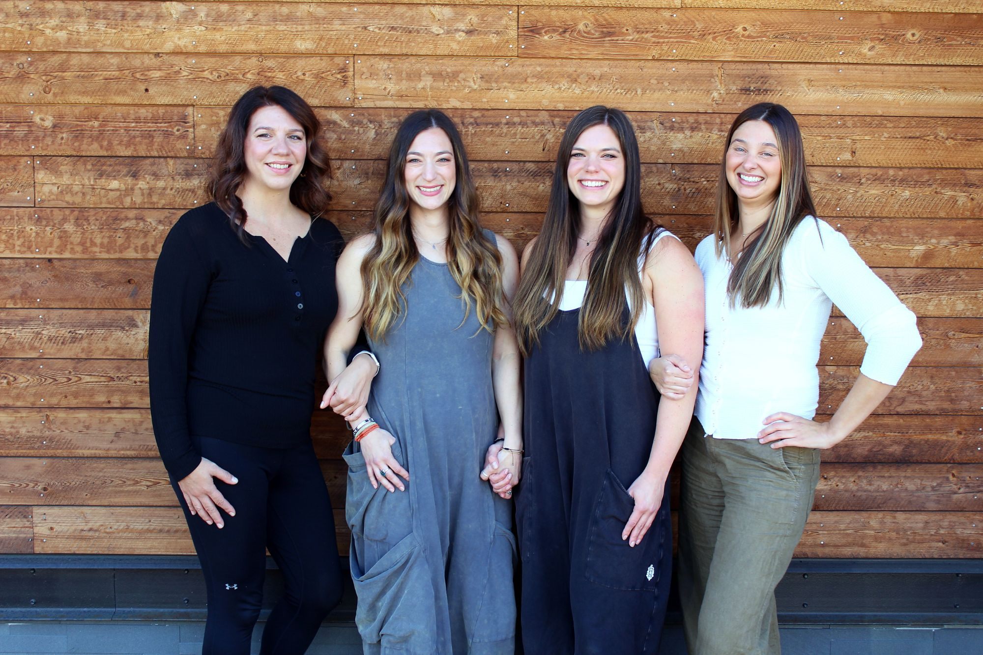 The Powerful Women's Health team standing arm in arm in front of a wood wall